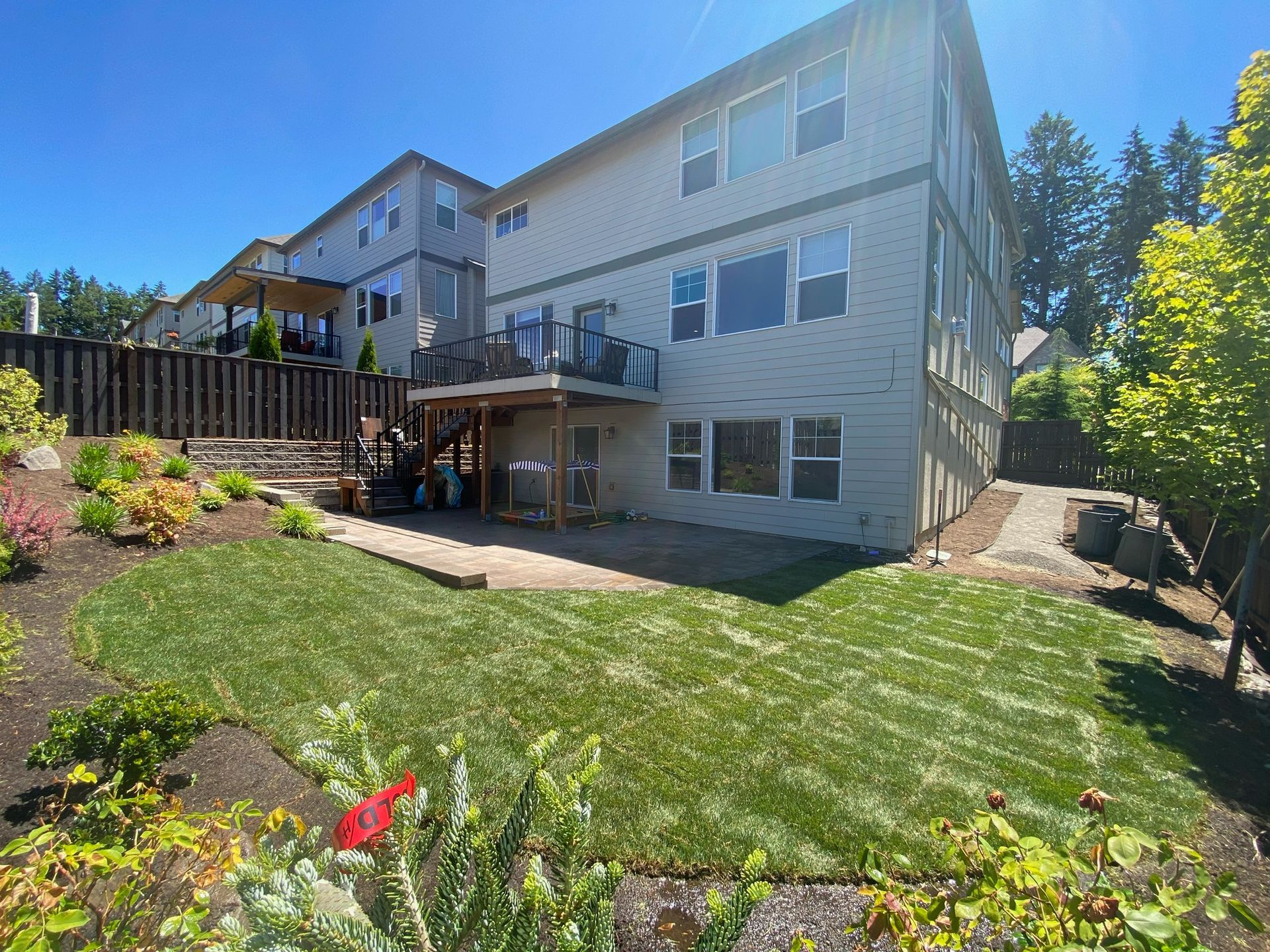 Backyard with green lawn, deck, and a beige house on a sunny day