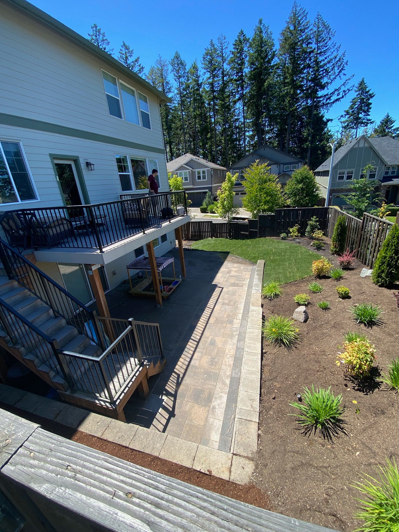 Backyard with raised deck, brick patio, and landscaped garden beds beside a white house