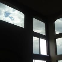 A room with a lot of windows and a cloudy sky behind them.