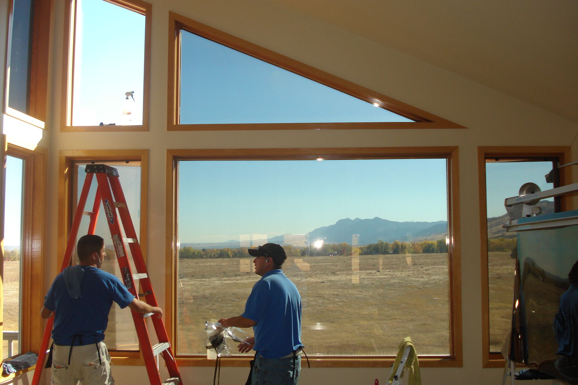 Two men are working on a large window in a house.
