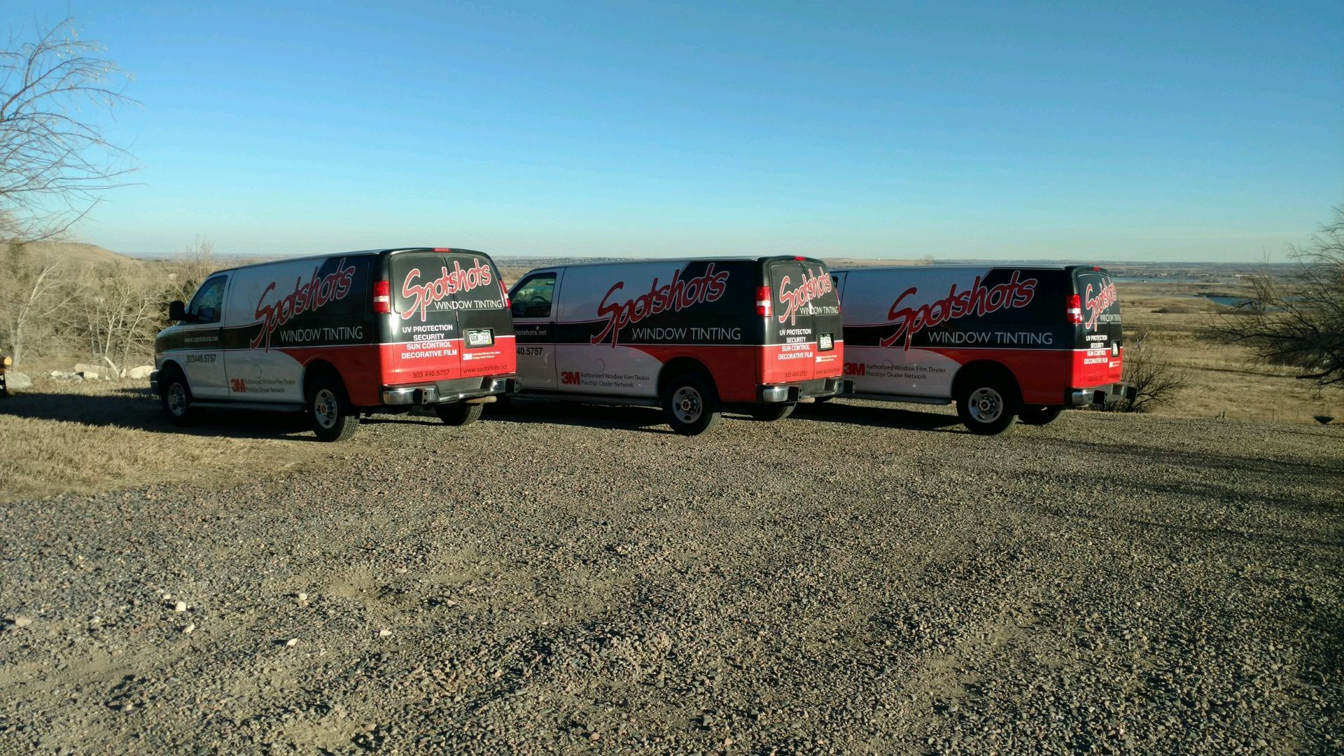 Three red and white vans are parked on a gravel road.