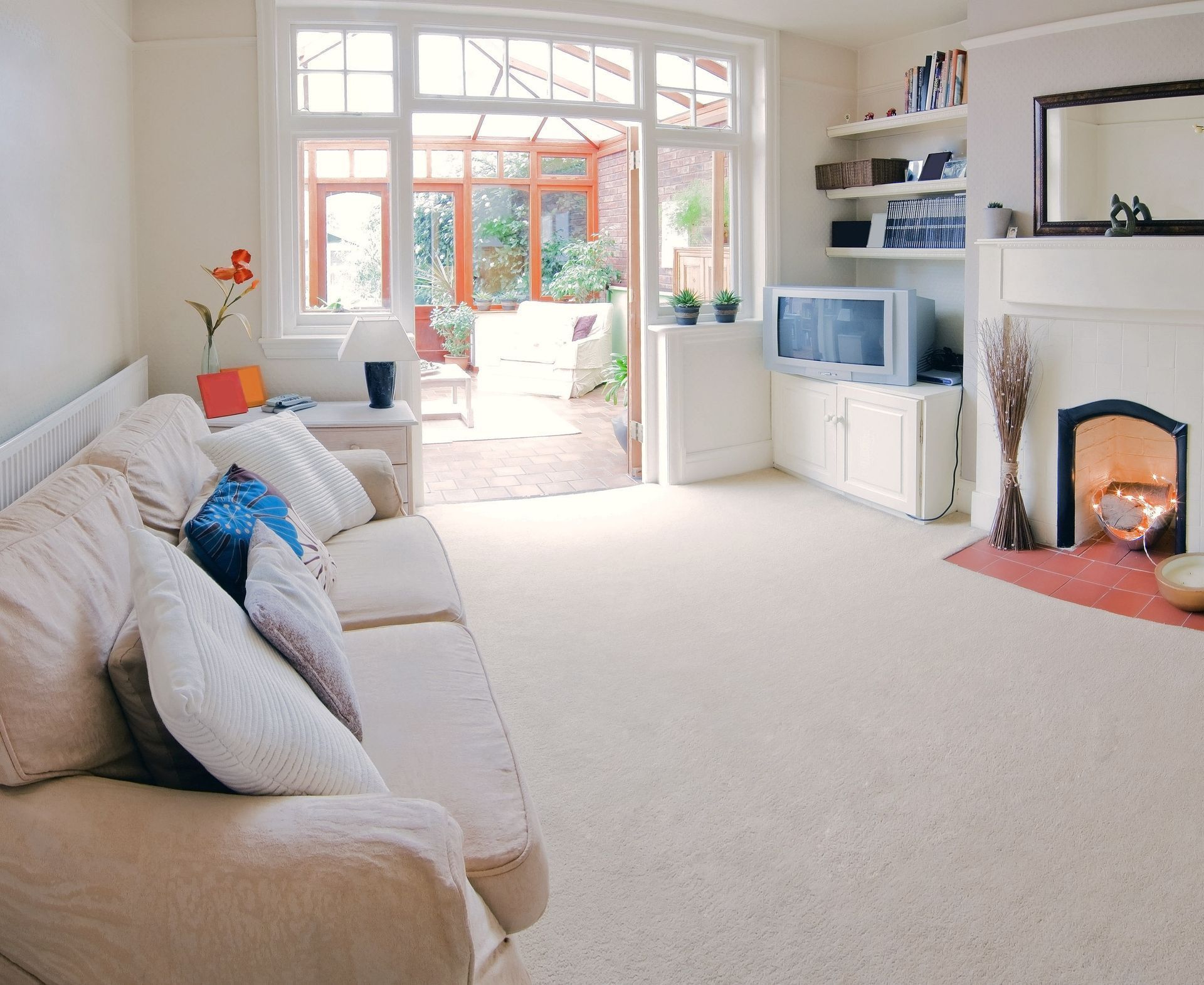 Cozy living room with cream-colored sofa, fireplace, and open glass doors leading to a sunroom and garden.