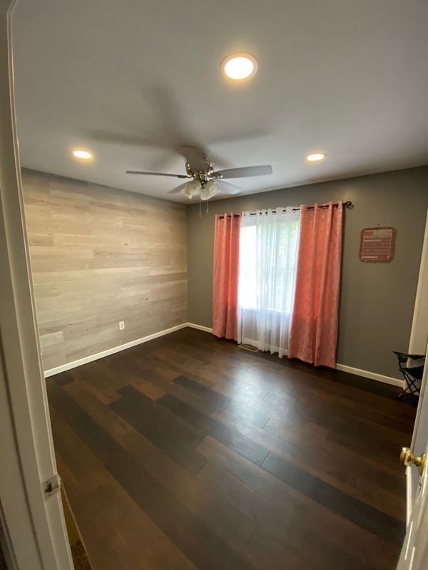 Bedroom with wood-look accent wall, dark wood floor, window with pink curtains.