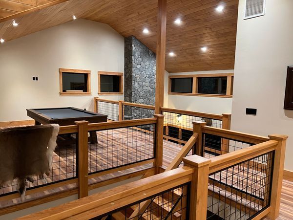 Interior view of a rustic game room with pool table, wood beams, stone fireplace, and metal railings.