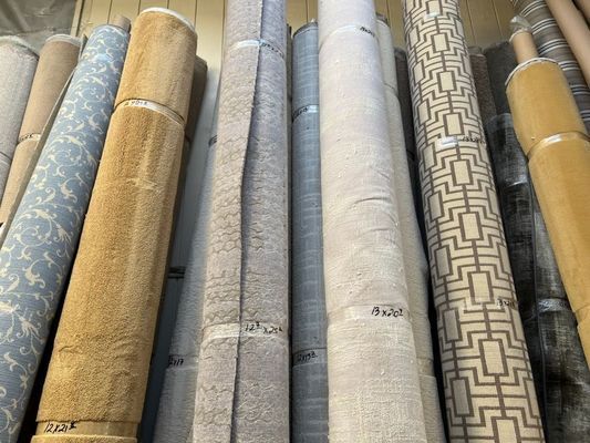 Rolls of various carpets, beige and patterned, stacked in a store.