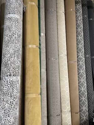 Rolled-up carpet samples in various colors and patterns displayed side by side; beige, gray, patterned, and solid.
