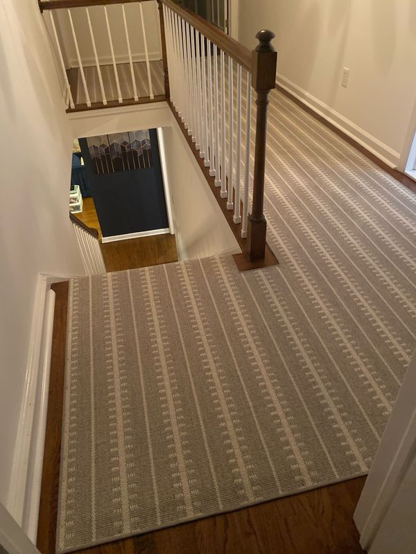 Staircase with gray patterned carpet, wooden railing and trim.