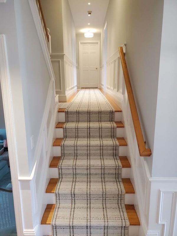 Staircase with patterned runner rug, light walls and trim, wooden handrail and steps.