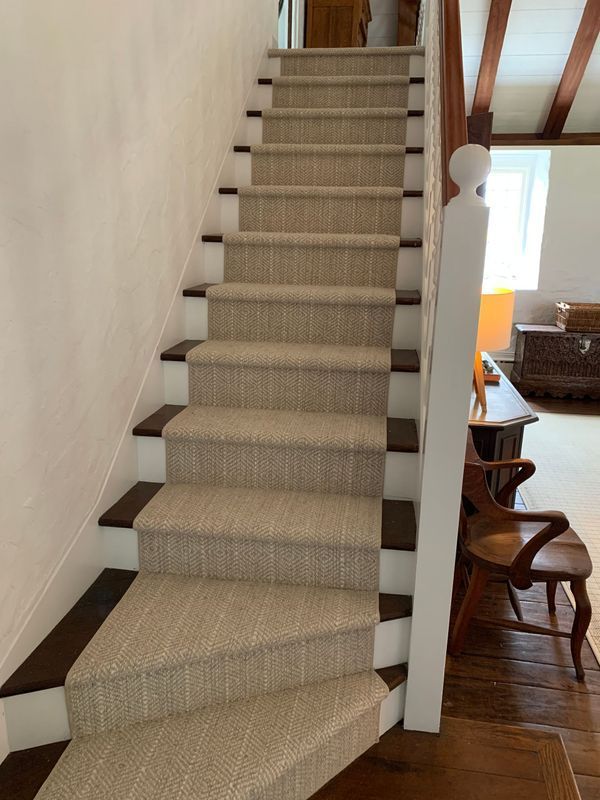 Staircase with carpeted steps and white risers, leading up to a landing. Brown wood trim and handrail.