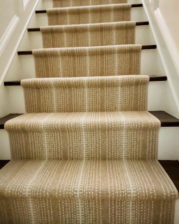 Beige carpet runner on a wooden staircase with white side panels.