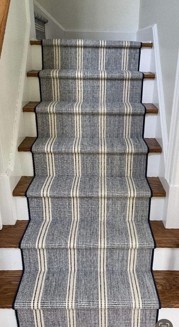 Staircase with grey plaid carpet runner, wood steps, white trim.