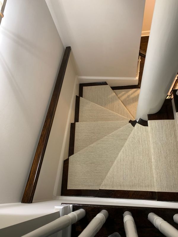 Staircase with light-colored carpet runner and dark wooden trim. White walls and banister.