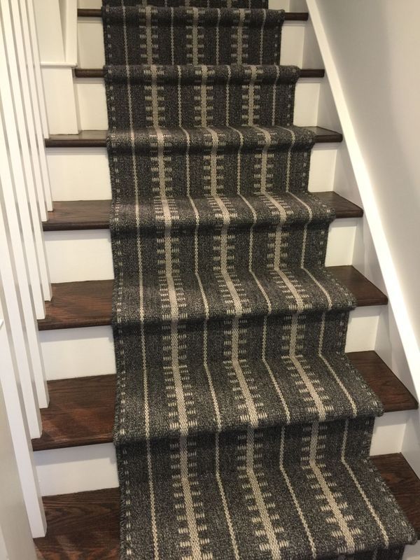 Staircase with patterned gray and beige carpet runner, wooden steps, and white banister.