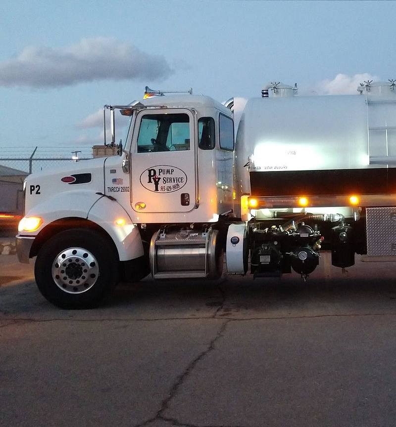 White semi-truck with a silver tank, parked outside at dusk. The truck has the logo