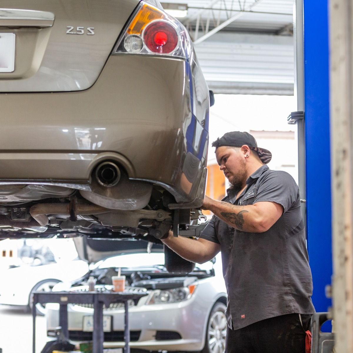 Mechanic working on the underside of a car raised on a lift in a garage.