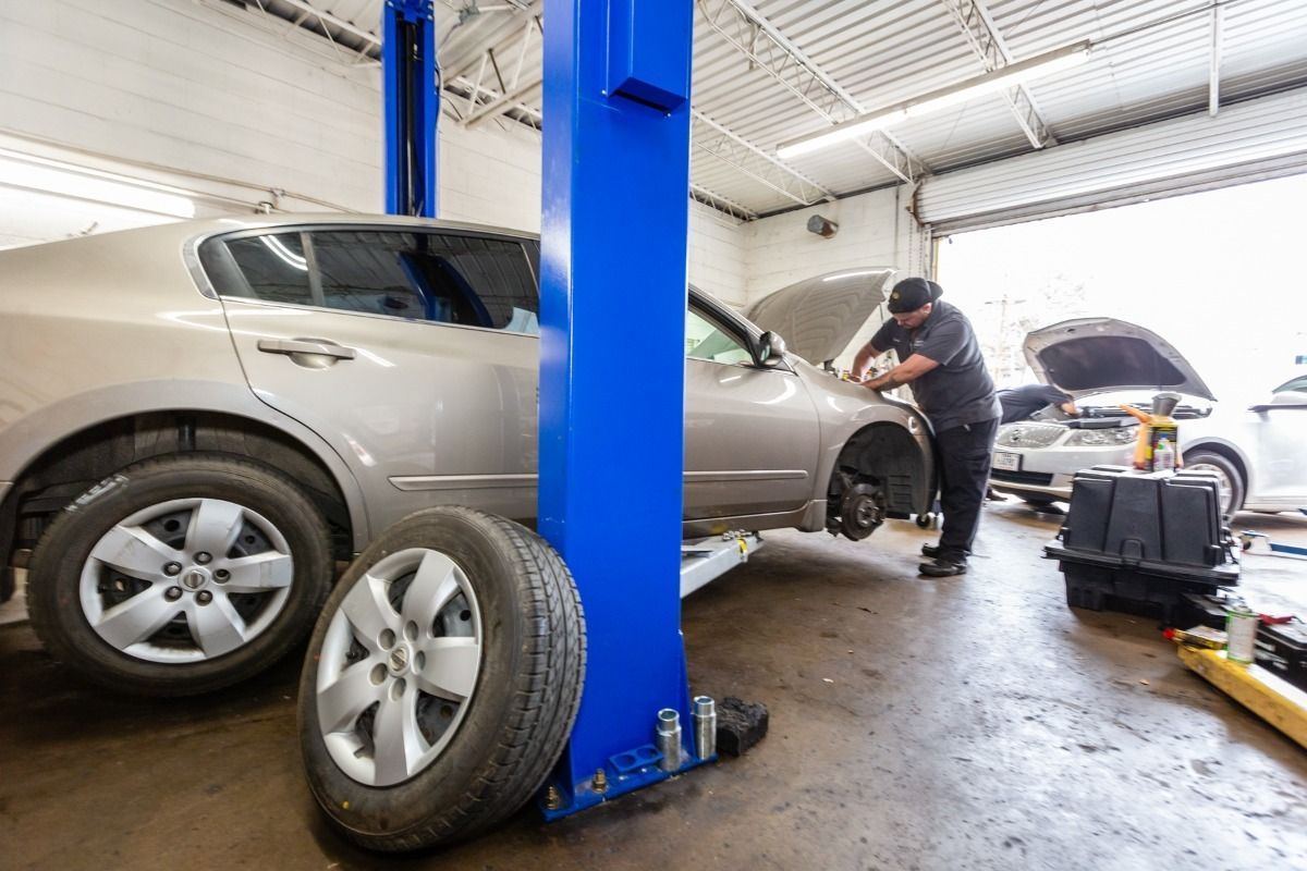 Mechanic working on car raised on a lift in a garage; spare tire on floor.