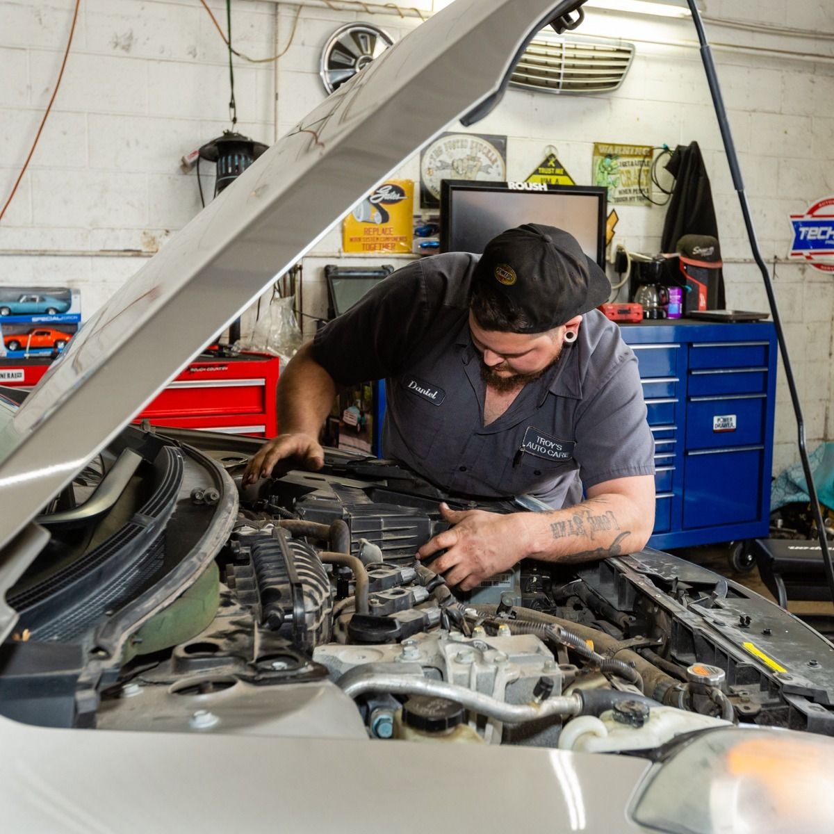 Mechanic working on a car engine in a garage. Gray car, blue tool cabinet, and open hood.