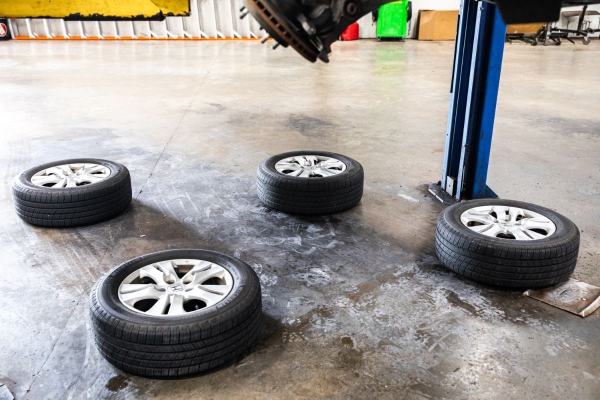 Four car tires on a garage floor, with a car's wheel hub lifted in the background.