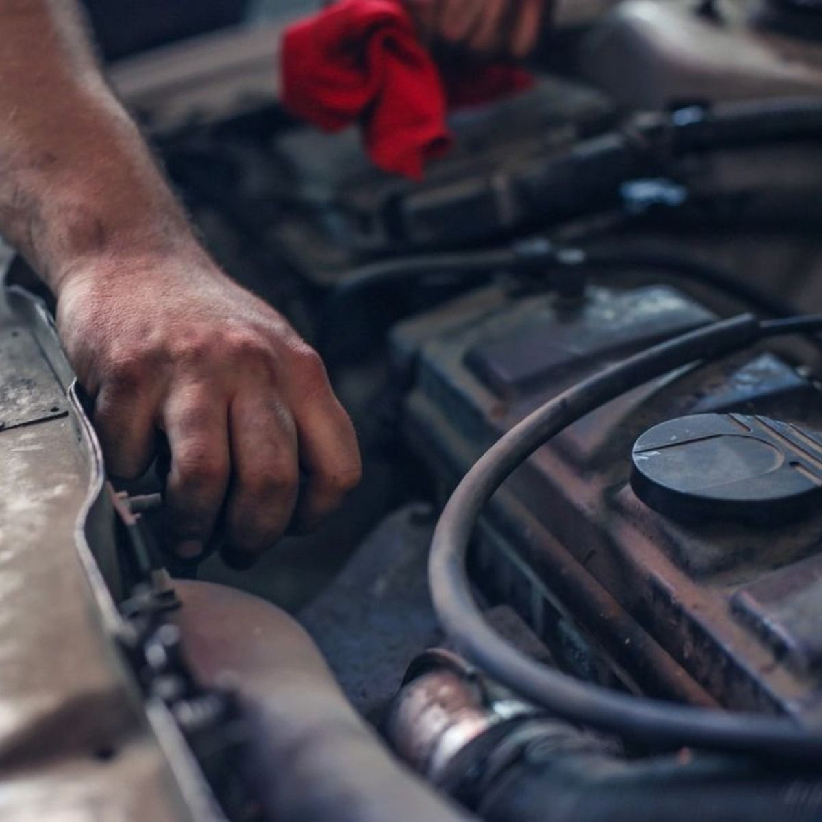 Mechanic's hand working on a car engine; a red rag is visible in the background.