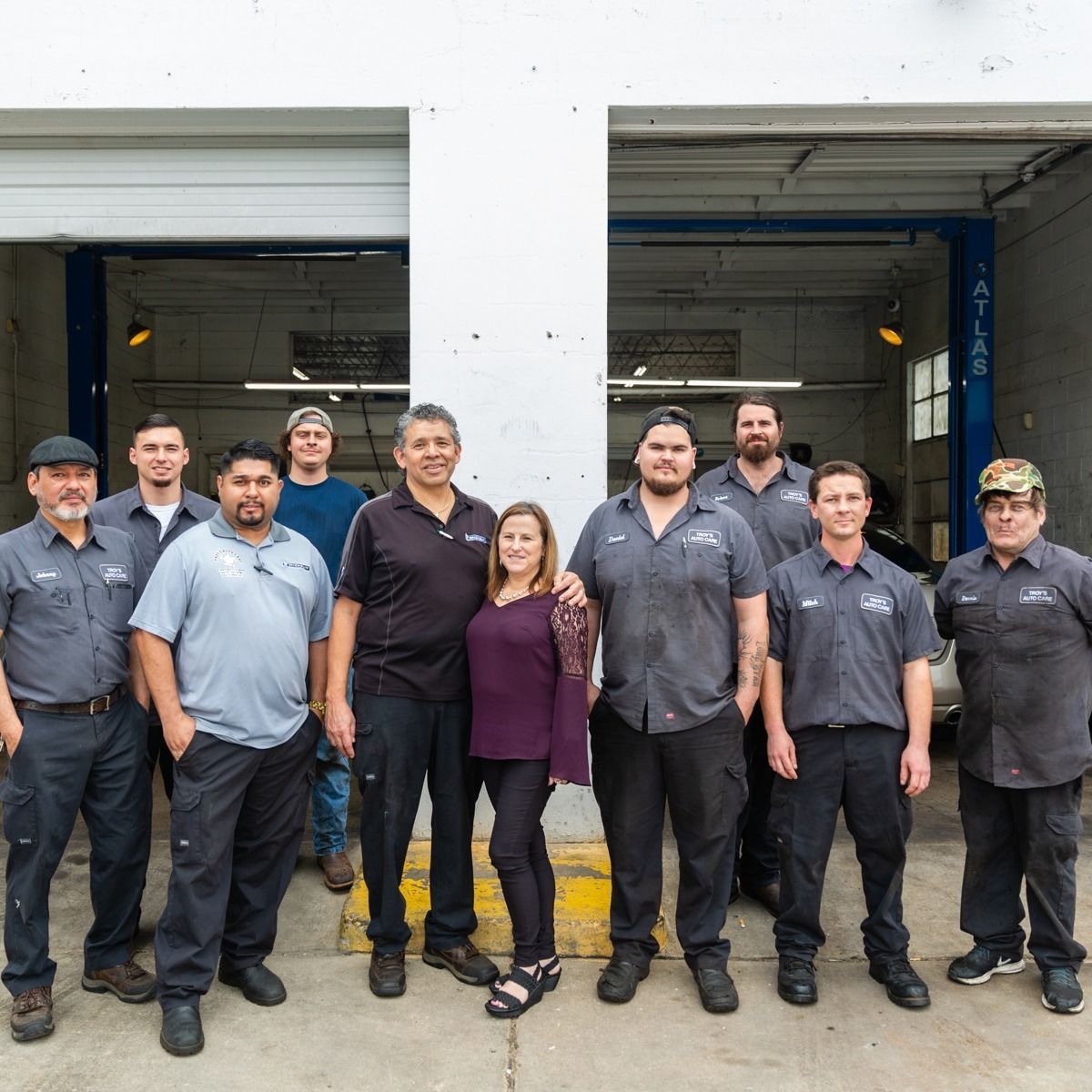 Group of auto shop employees posing in front of garage door.
