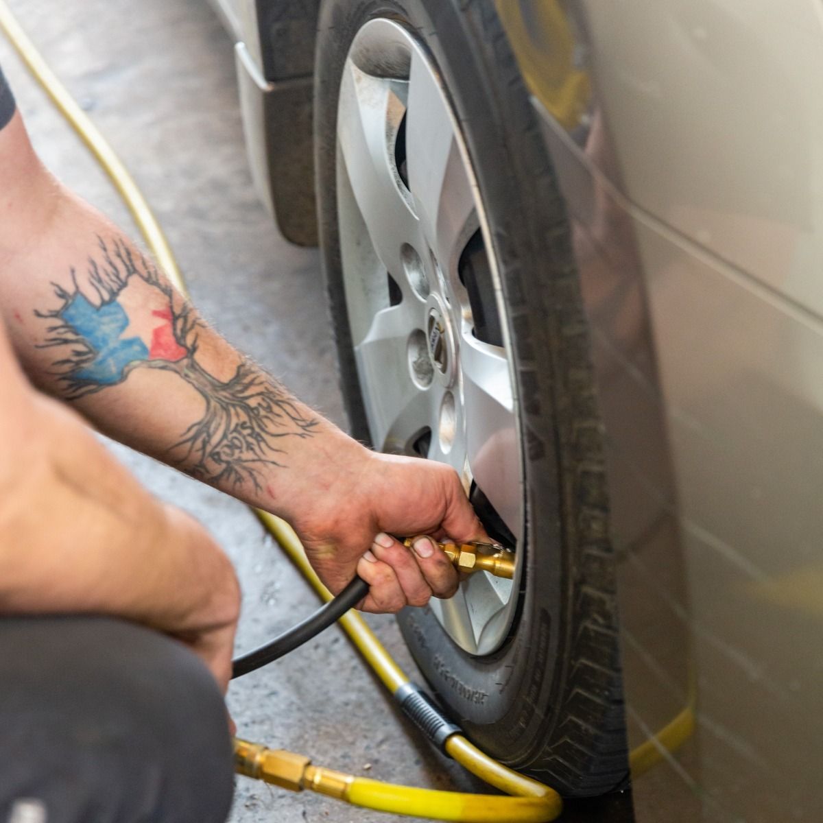 Person filling car tire with air. Close-up of arm with tattoo. Yellow air hose.