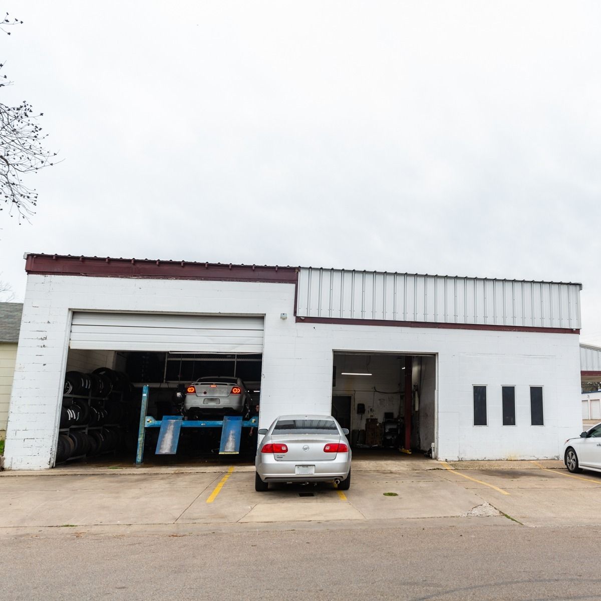 White auto repair shop with two bays open, car on a lift, and car parked outside.