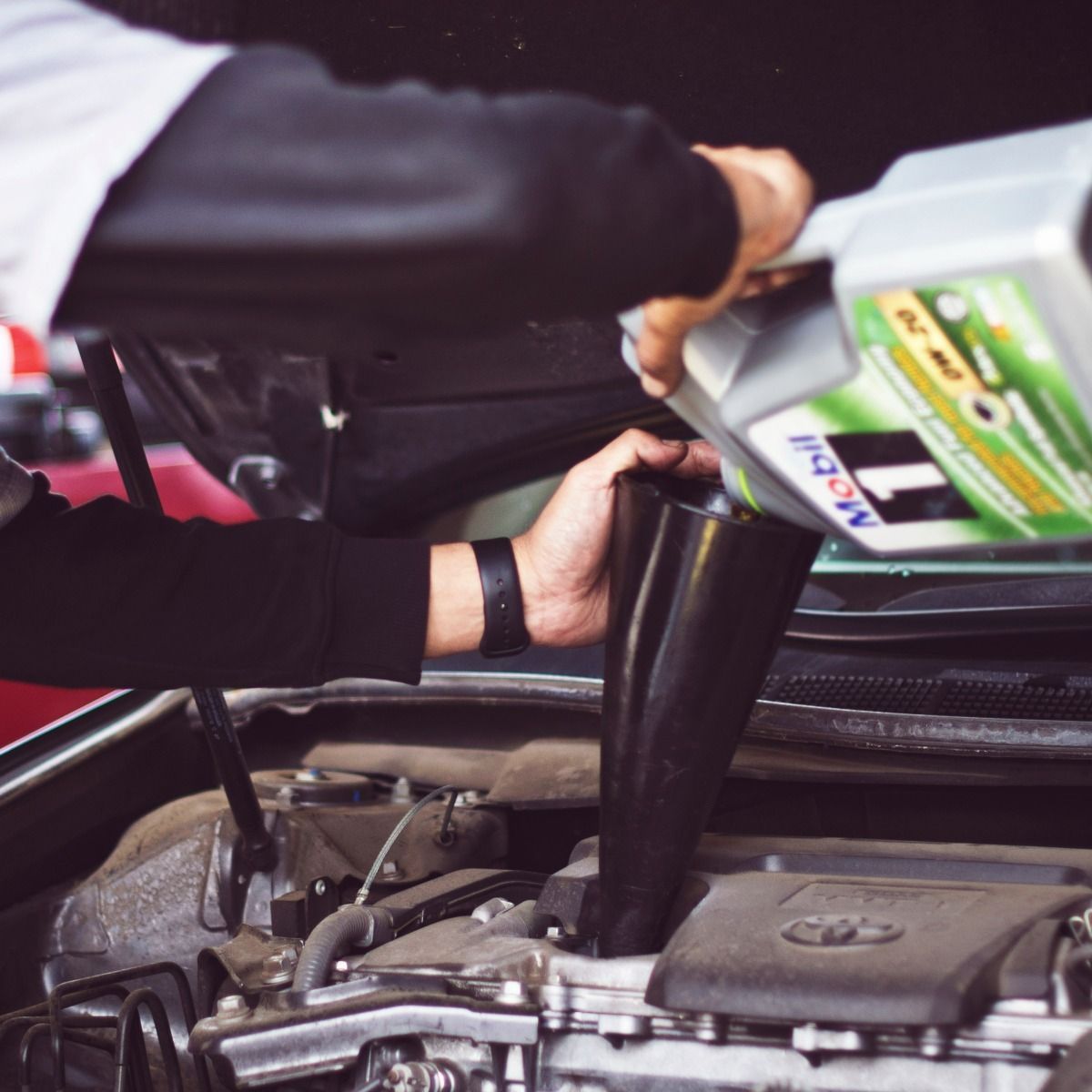 Person pouring oil into a car engine with a funnel.