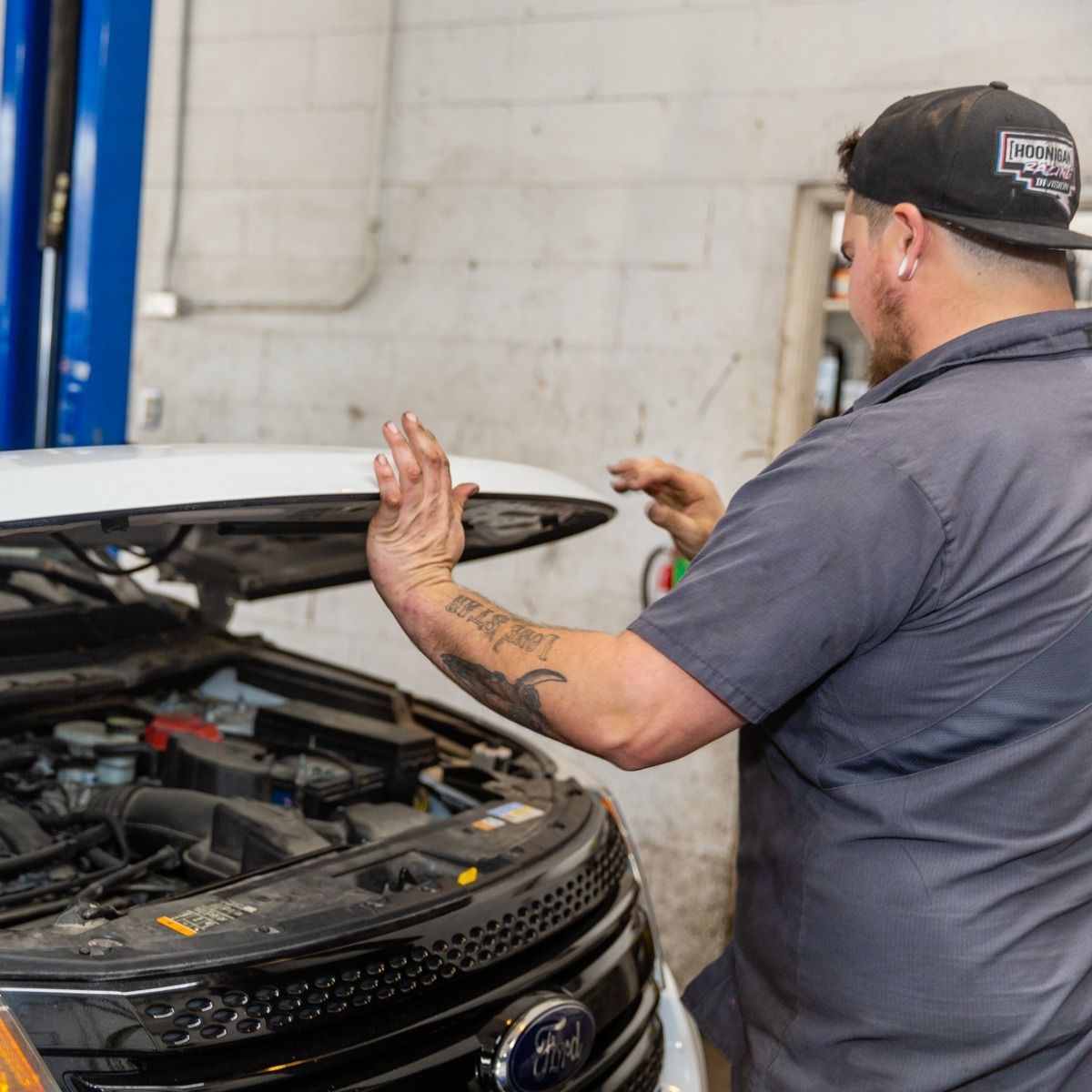 Mechanic opening the hood of a white car in a garage.