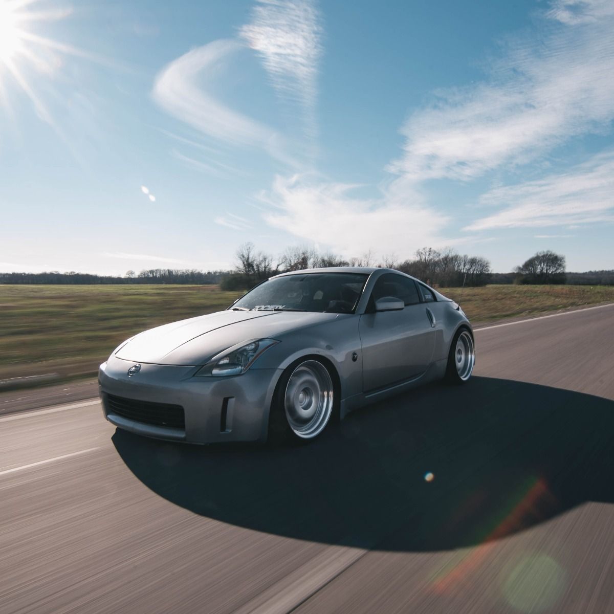 Silver Nissan 350Z sports car on a road, sunny day.