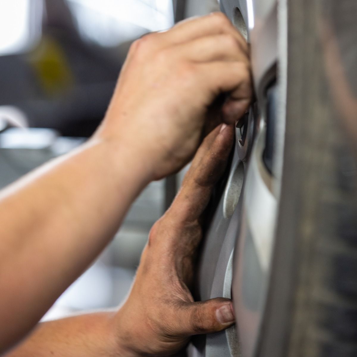 Hands installing a tire on a silver rim. Mechanic's hands are dirty.