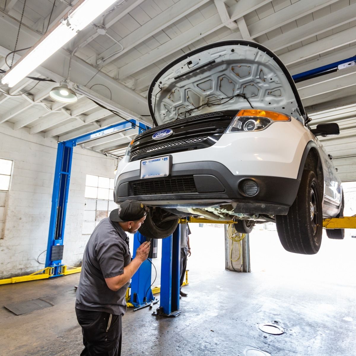 Mechanic inspecting a white SUV lifted on a blue hydraulic lift in a repair shop.