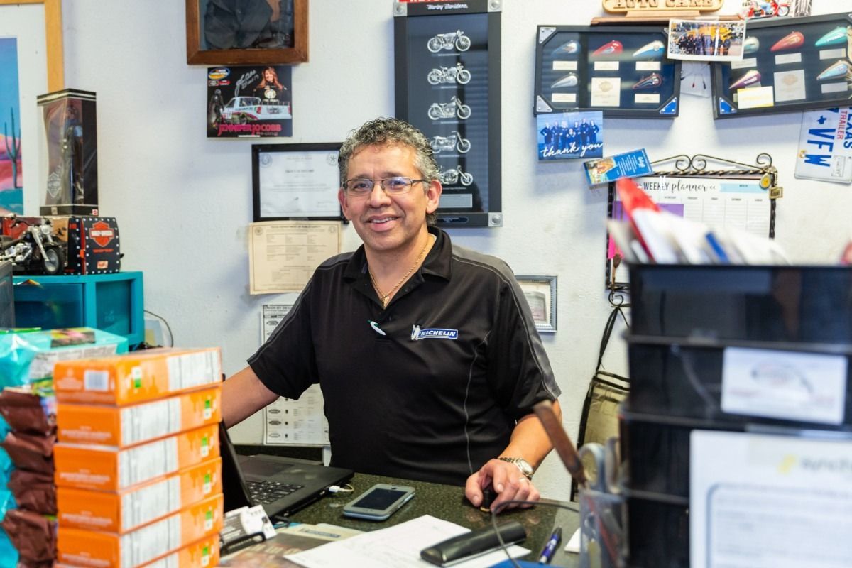 Man in black shirt smiles, stands behind counter in an auto shop.