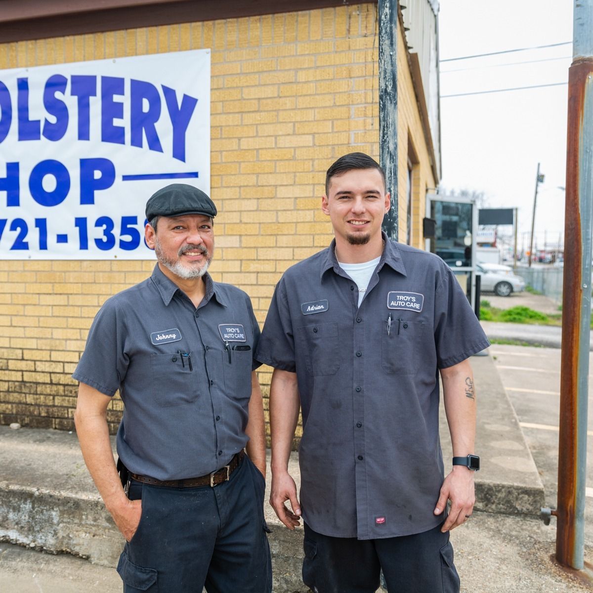 Two men in grey work shirts stand outside an 