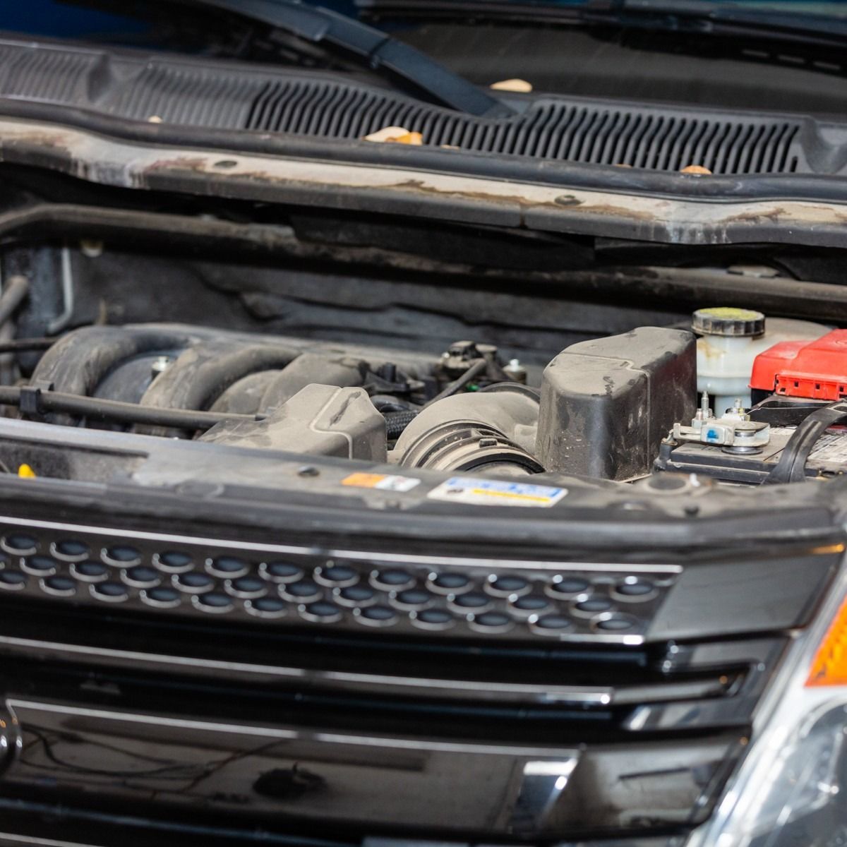 Car engine bay, open, showing components; dusty and slightly dirty with battery visible.