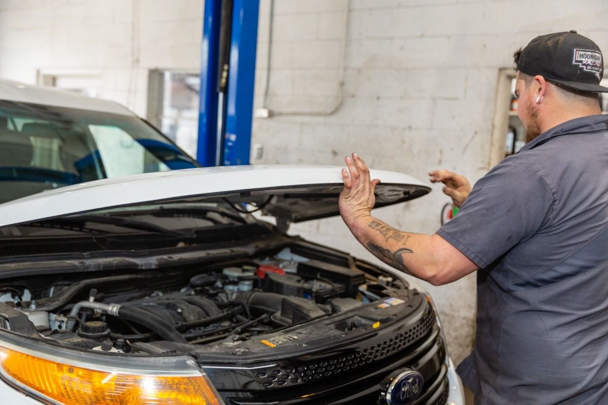 Mechanic opening the hood of a white car in a garage.