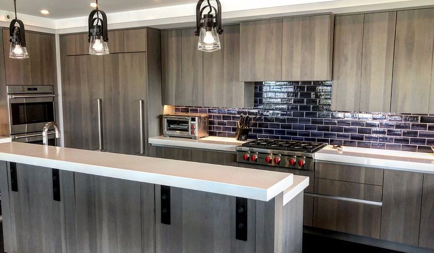 Modern kitchen with light wood cabinets, white countertops, stainless steel appliances, and a dark blue tiled backsplash.