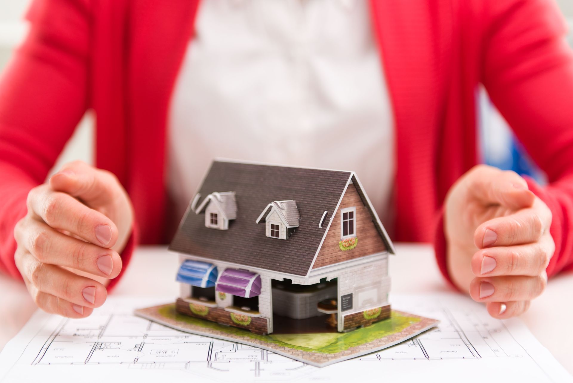 Hand holding a magnifying glass in front of a house, possibly for inspection.