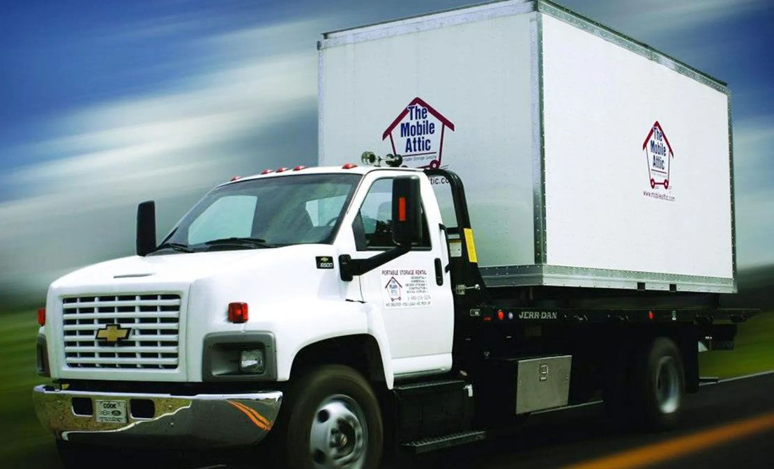 White box truck driving on a road under a cloudy sky