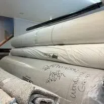 Large rolls of off-white carpet stacked in a room. Some rolls have handwritten labels.
