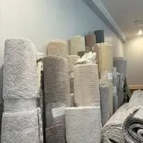 Various rolled-up beige and tan carpets stacked in a room.