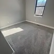 Empty room with gray carpet, a window, and sunlight.