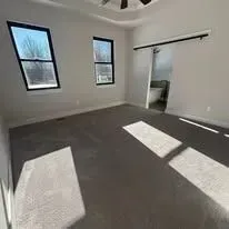 Empty room with two windows, a sliding door, and grey carpet.