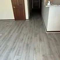 Light gray wood-look flooring extends to a brown wooden door and white countertop.