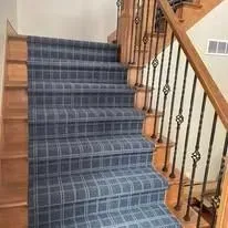 Blue plaid carpeted staircase with wooden banister and railing.