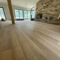 Light wood floor in a spacious room, leading towards a stone fireplace.
