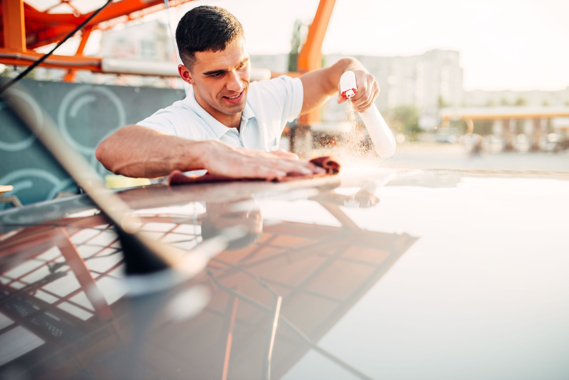 Man sprays cleaner onto car roof and wipes with a cloth.