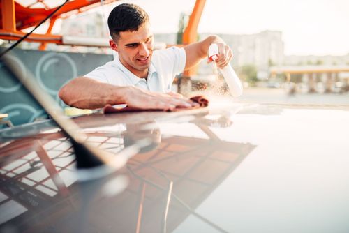 Man sprays cleaner onto car roof and wipes with a cloth.