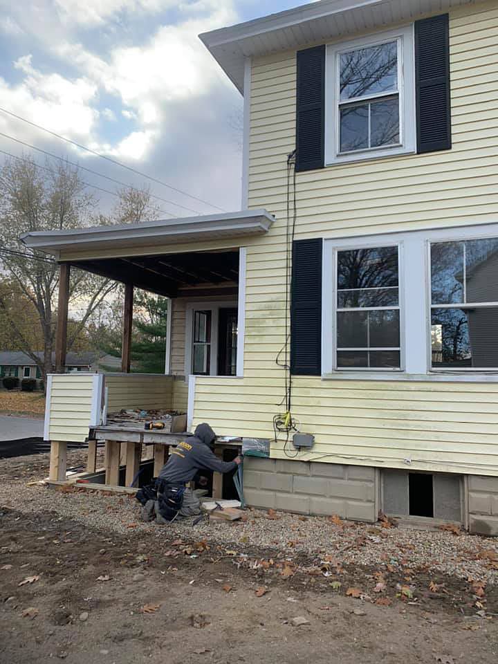 A man is kneeling in front of a yellow house with black shutters.