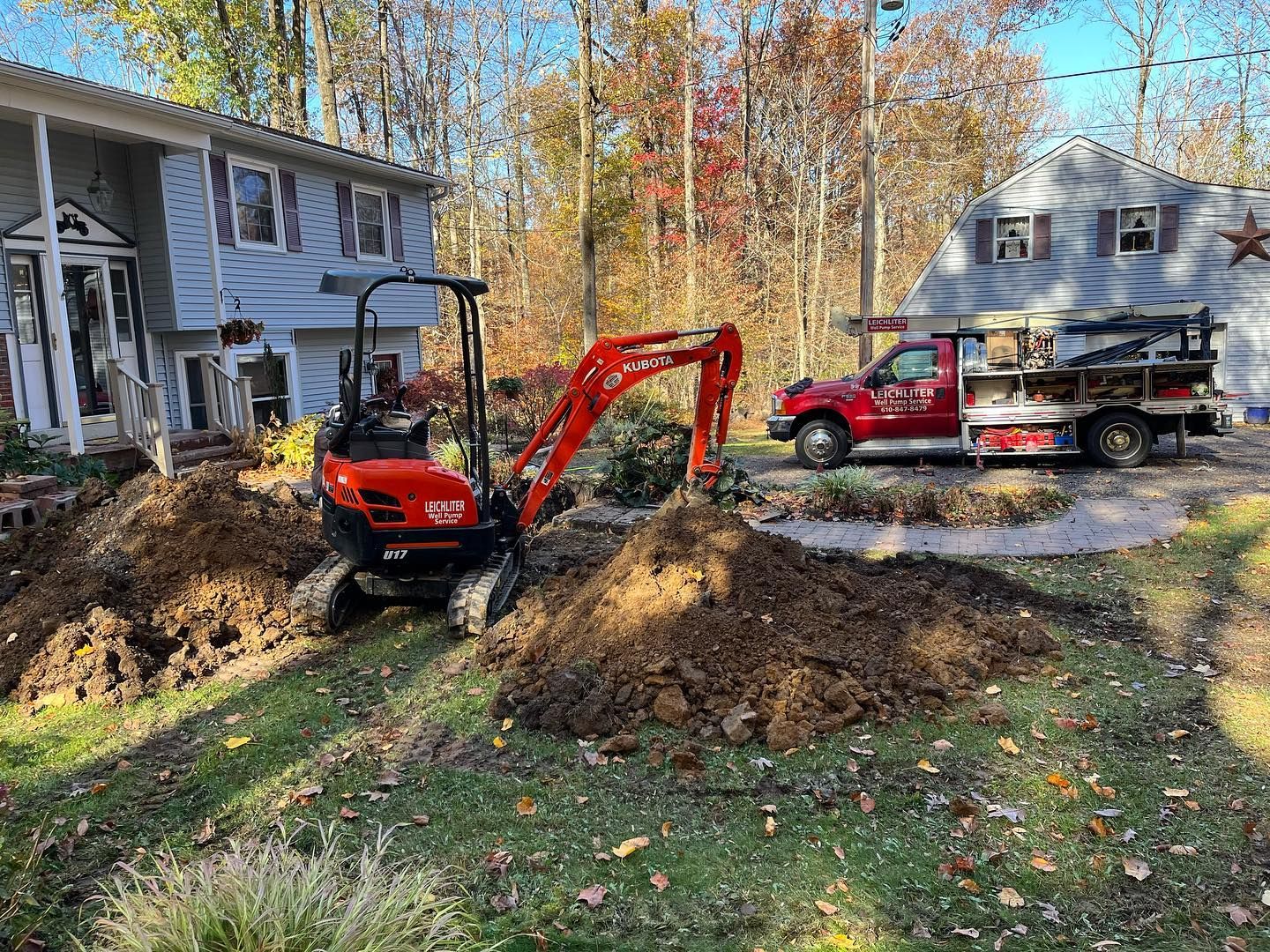 A red excavator is digging a hole in front of a house.