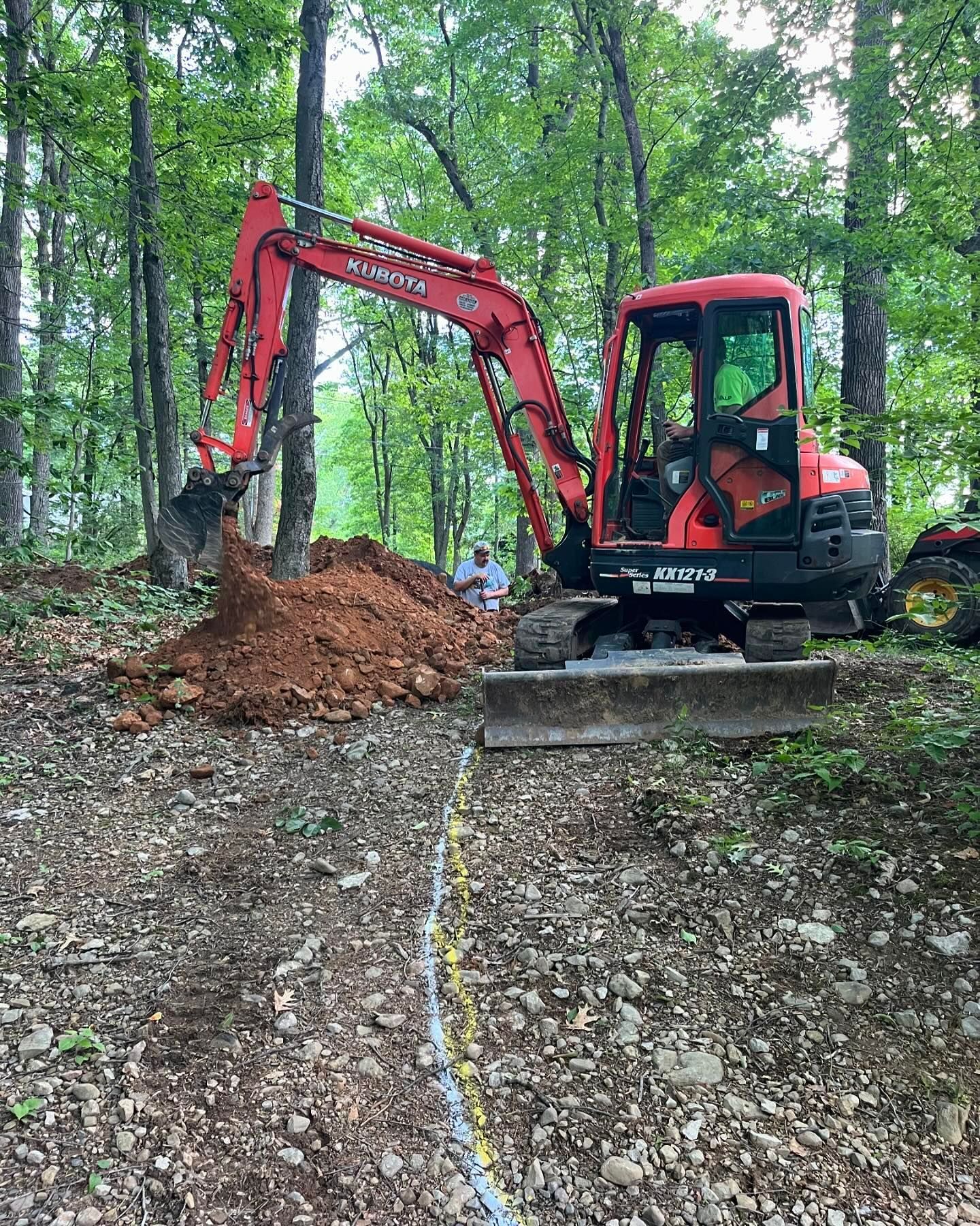 A red excavator is digging a hole in the woods.